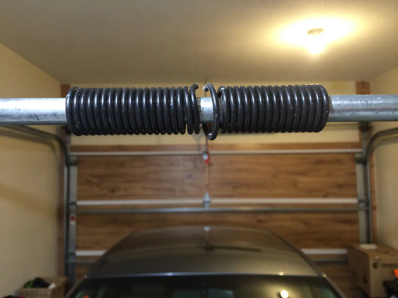 A broken torsion spring is on a metal rod above a garage door.